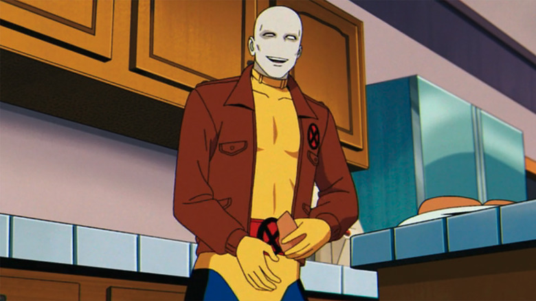 An image of Morph from X-Men 97 in their yellow costume with a brown X jacket over it. They're sporting their new look, genderless with gray/white skin.